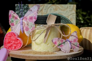 A cozy display featuring yellow bath salts in a jar, surrounded by decorative butterflies, essential oil, and colorful bath salt crystals