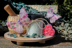 A cozy display featuring white bath salts in a jar, surrounded by decorative butterflies, essential oil, and colorful bath salt crystals