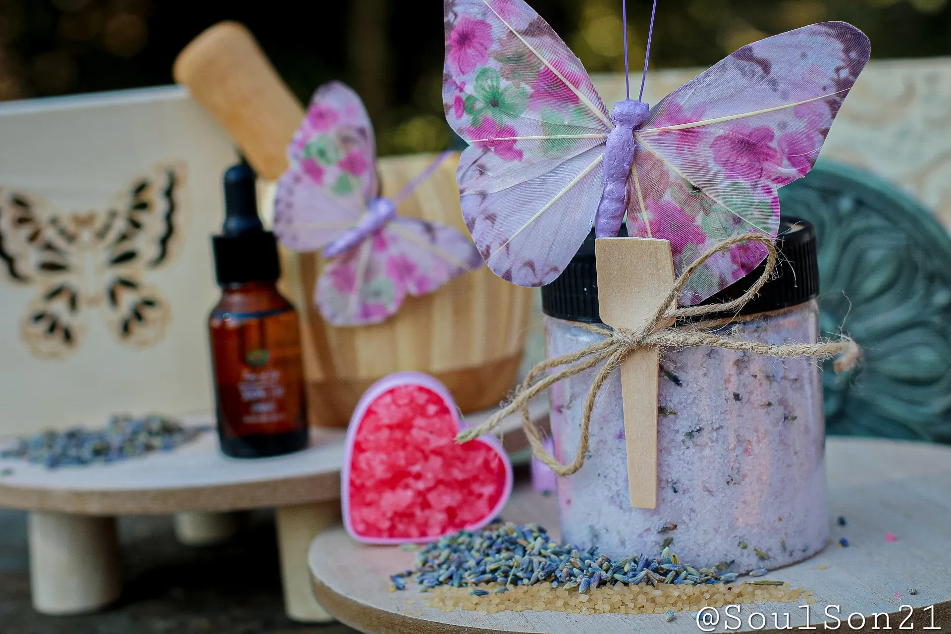 A cozy display featuring lavender bath salts in a jar, surrounded by decorative butterflies, essential oil, and colorful bath salt crystals