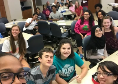 Group of students smiling for a selfie in a classroom with a CPR baby mannequin on the table
