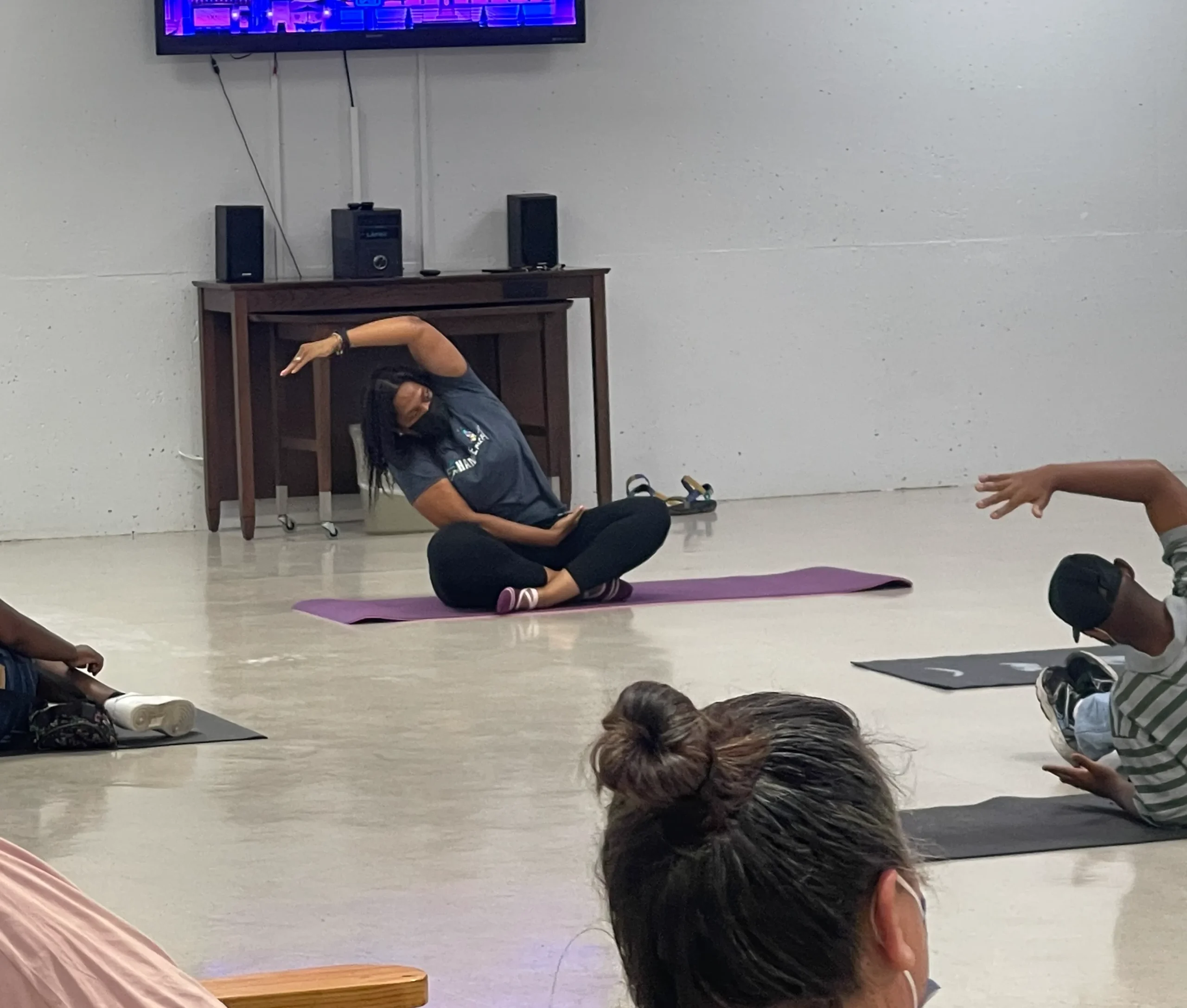 Instructor leading a yoga class, sitting on a mat and stretching with participants following