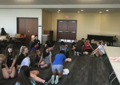 Students practicing CPR in groups on mannequins placed on the floor in a training room