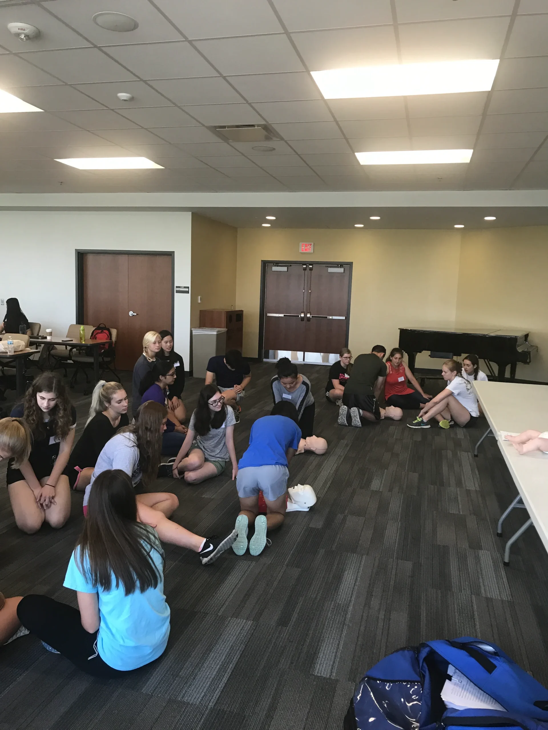 Students practicing CPR in groups on mannequins placed on the floor in a training room